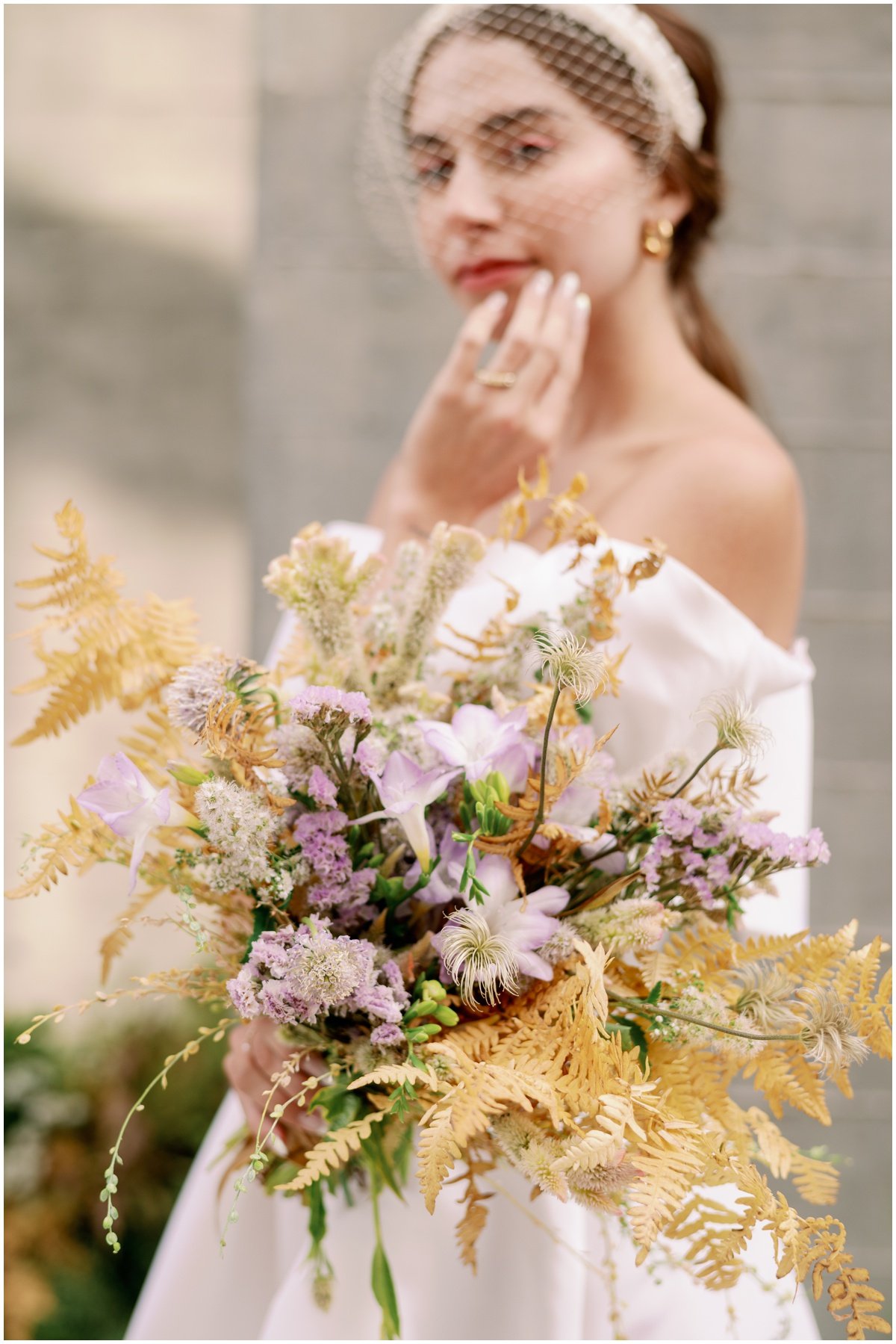 Bride wearing off the shoulder dress and headband carry bouquet of muted purple and yellow flowers | NKB Photo