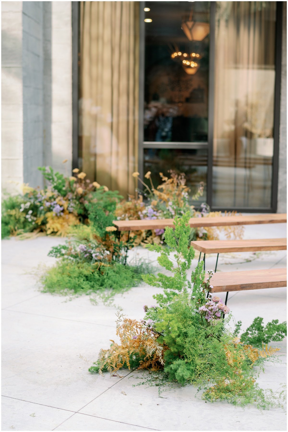 Ferns and yellow and purple floral arrangements lining wedding ceremony aisle | NKB Photo
