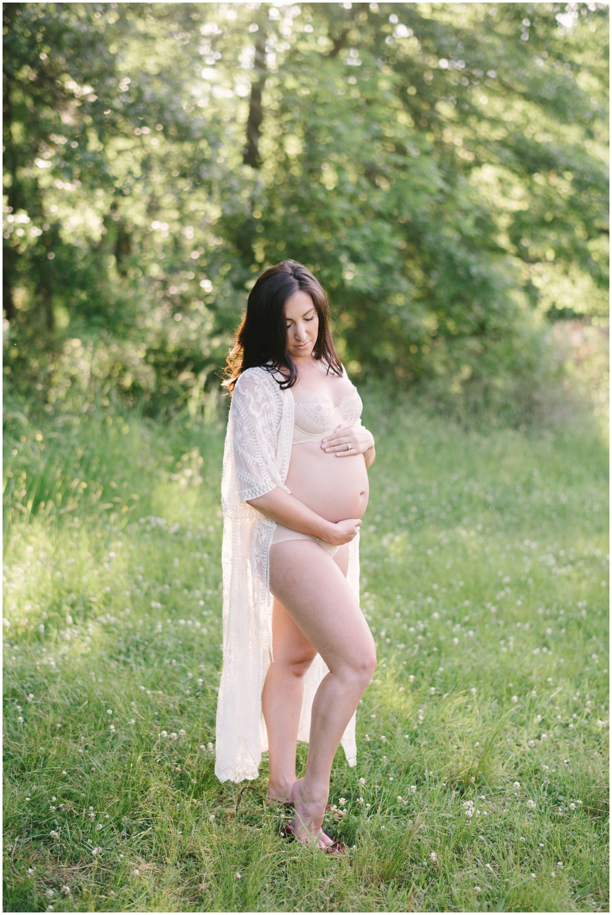 Woman standing in field looking down at pregnant belly during maternity session | NKB Photo