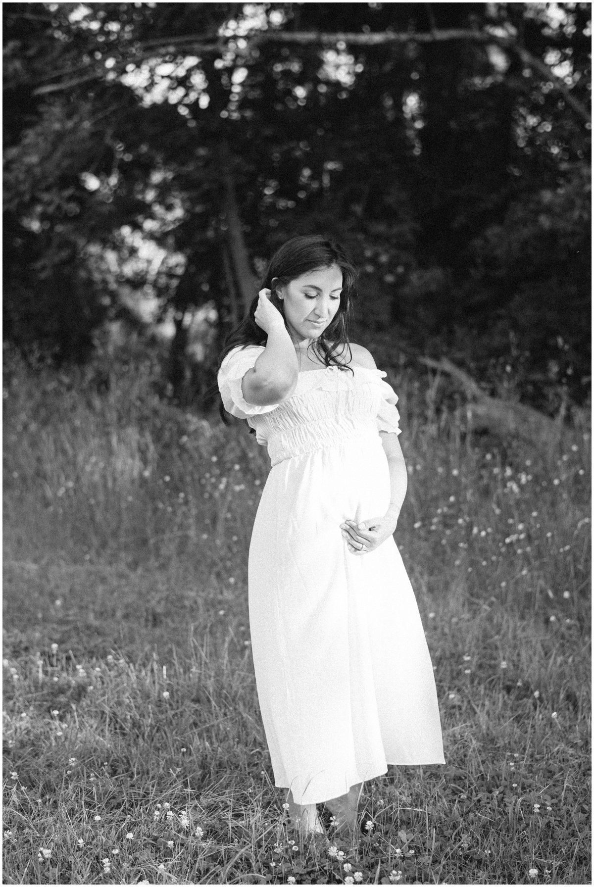 Woman tucking hair behind her ear and cradling baby bump during maternity session | NKB Photo