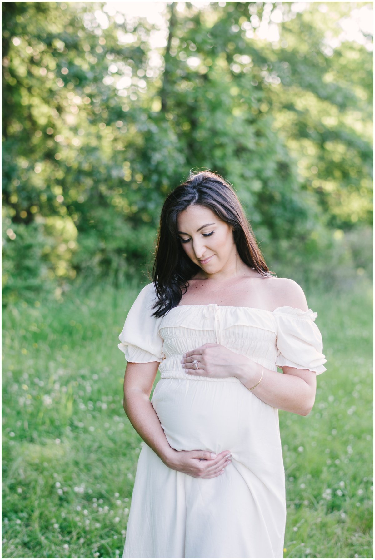 Woman wearing white flowy dress and cradling bump during maternity session | NKB Photo