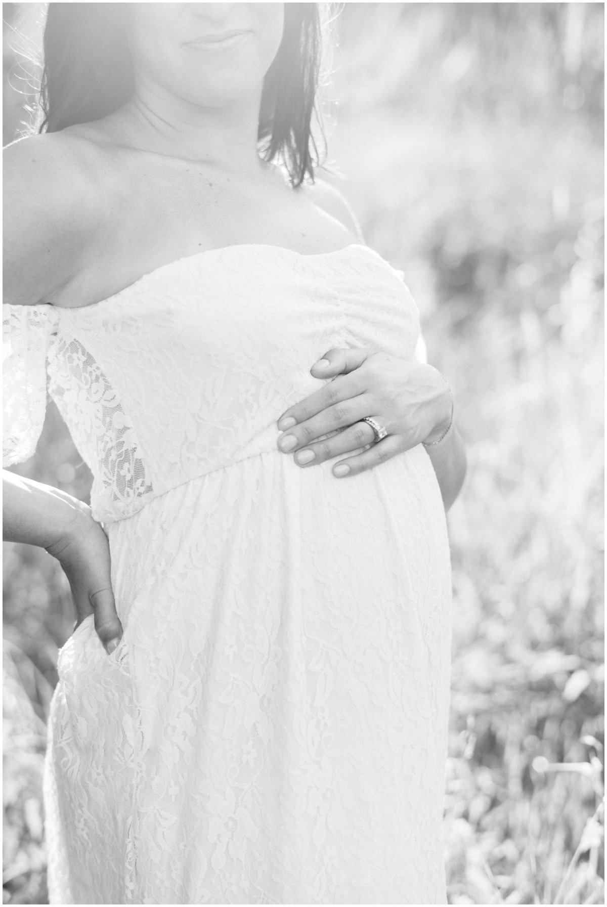 Woman wearing sleeveless white dress and cradling pregnant belly during maternity session | NKB Photo