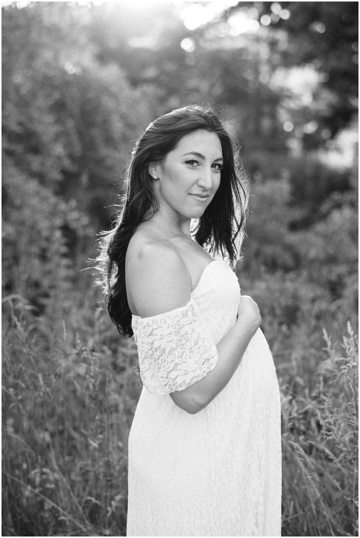 Woman wearing white flowy dress and cradling baby bump during maternity session | NKB Photo | Why maternity photos are important