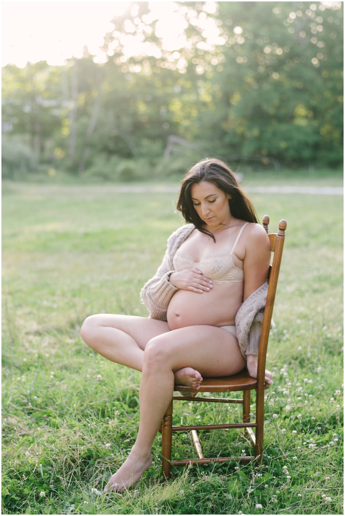 Woman sitting on chair and looking down at pregnant belly during maternity session | NKB Photo
