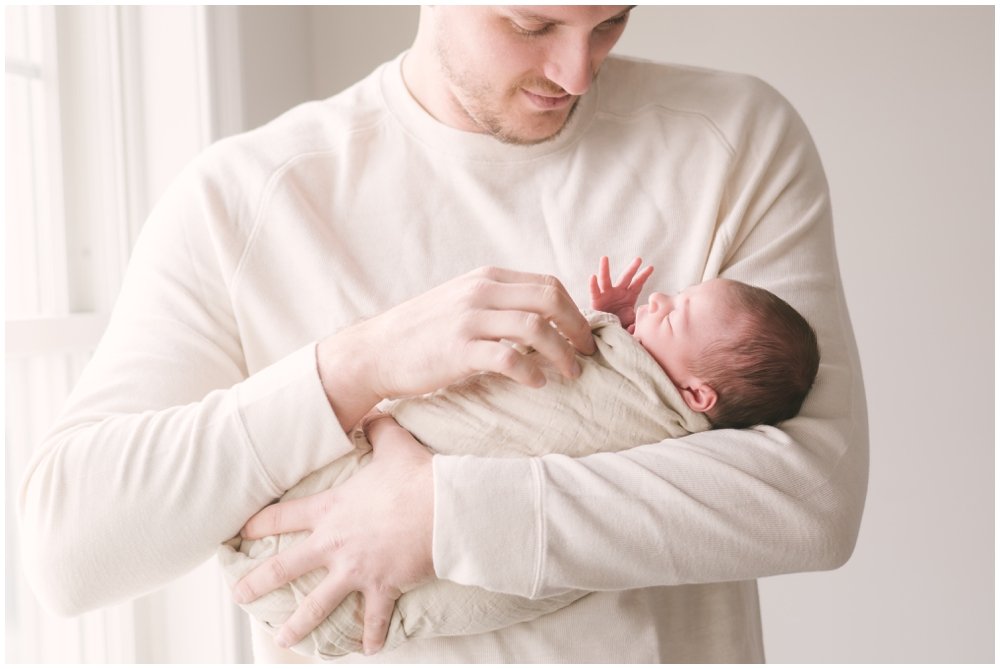 Dad holding and looking at swaddled newborn baby during session | NKB Photo