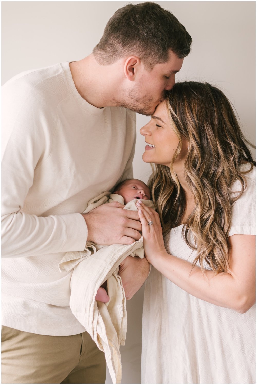 Dad holding newborn and kissing mom's head during newborn session | NKB Photo