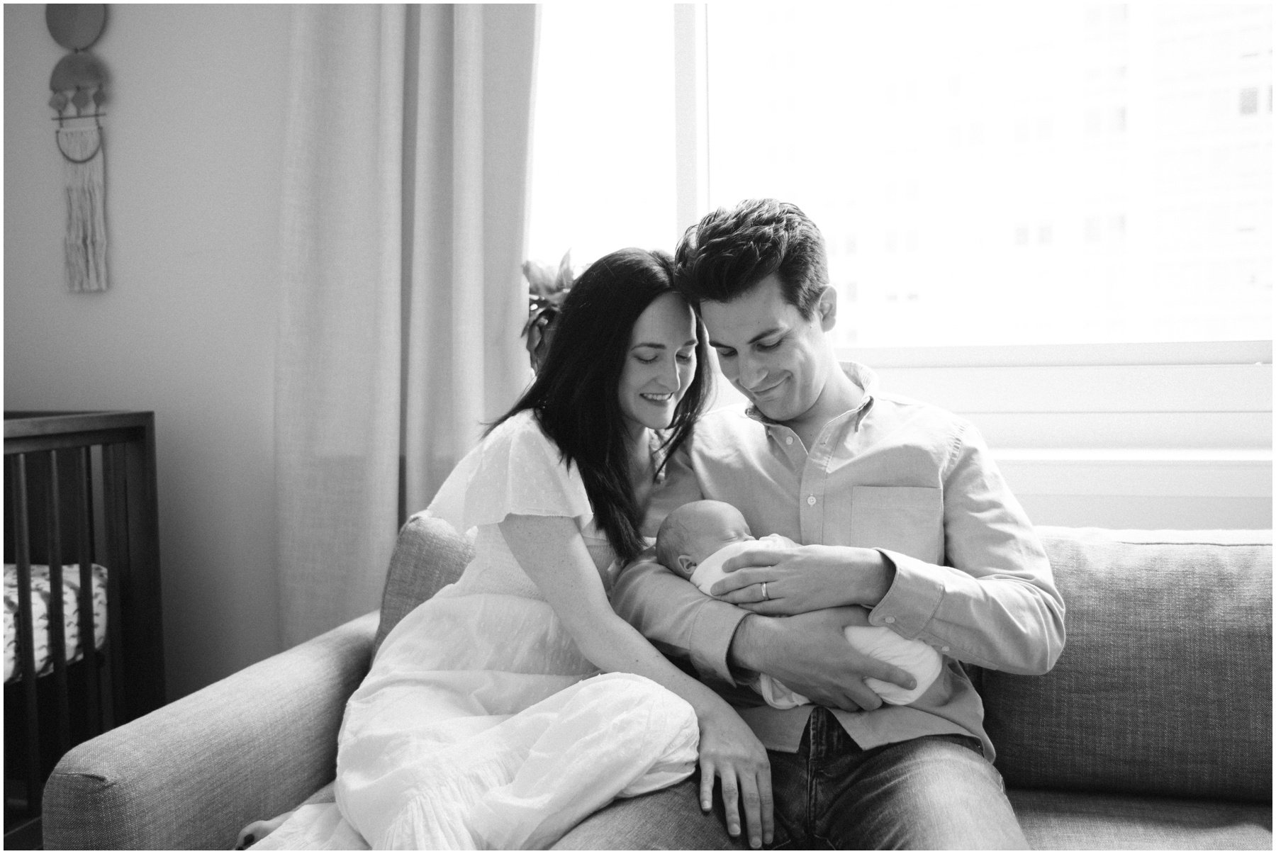 Mom and dad cuddling baby on couch during newborn session | NKB Photo