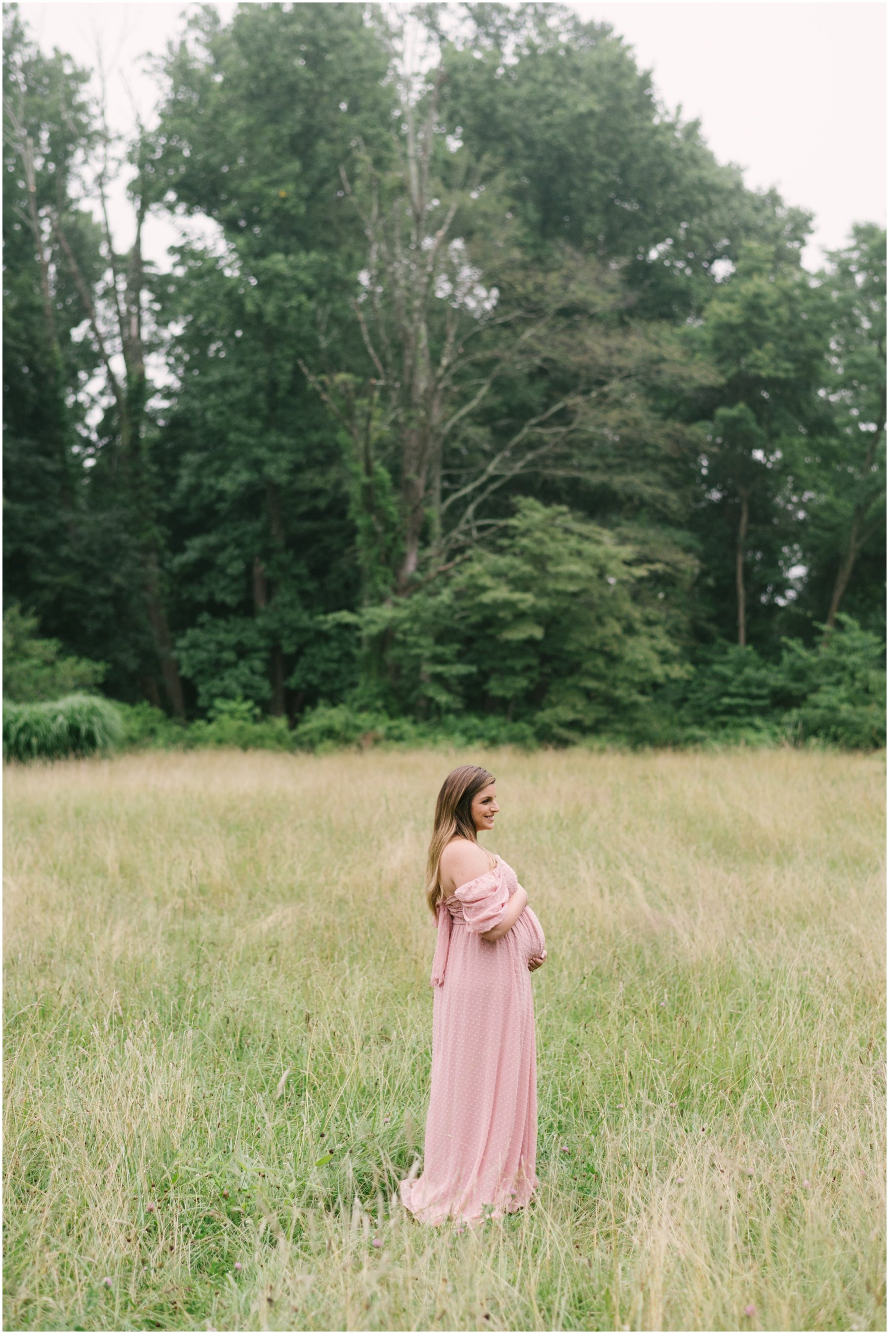 Woman standing in field looking off in distance during maternity session | NKB Photo