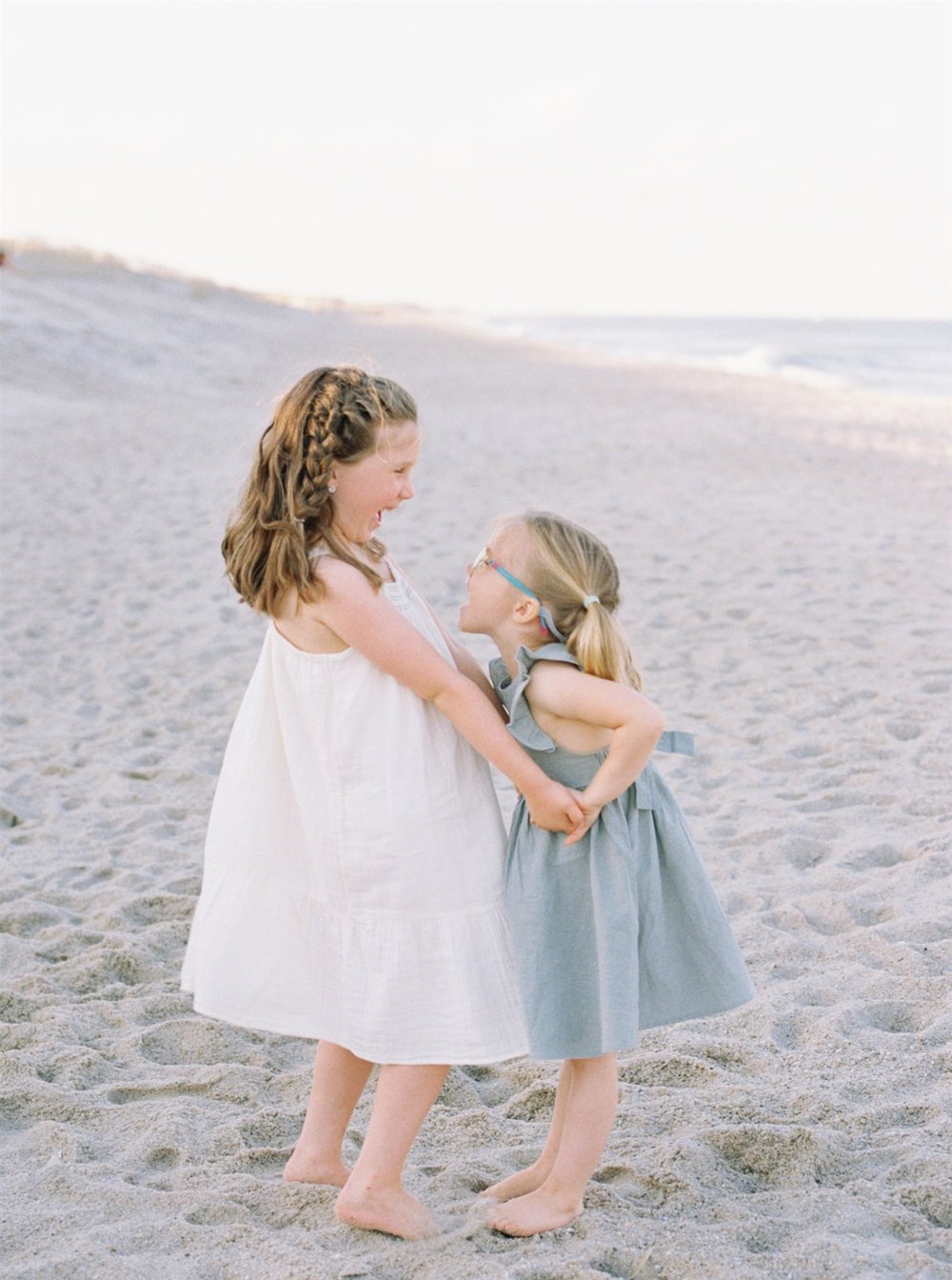 Sisters holding hands and laughing during Florida beach photo session  | NKB Photo