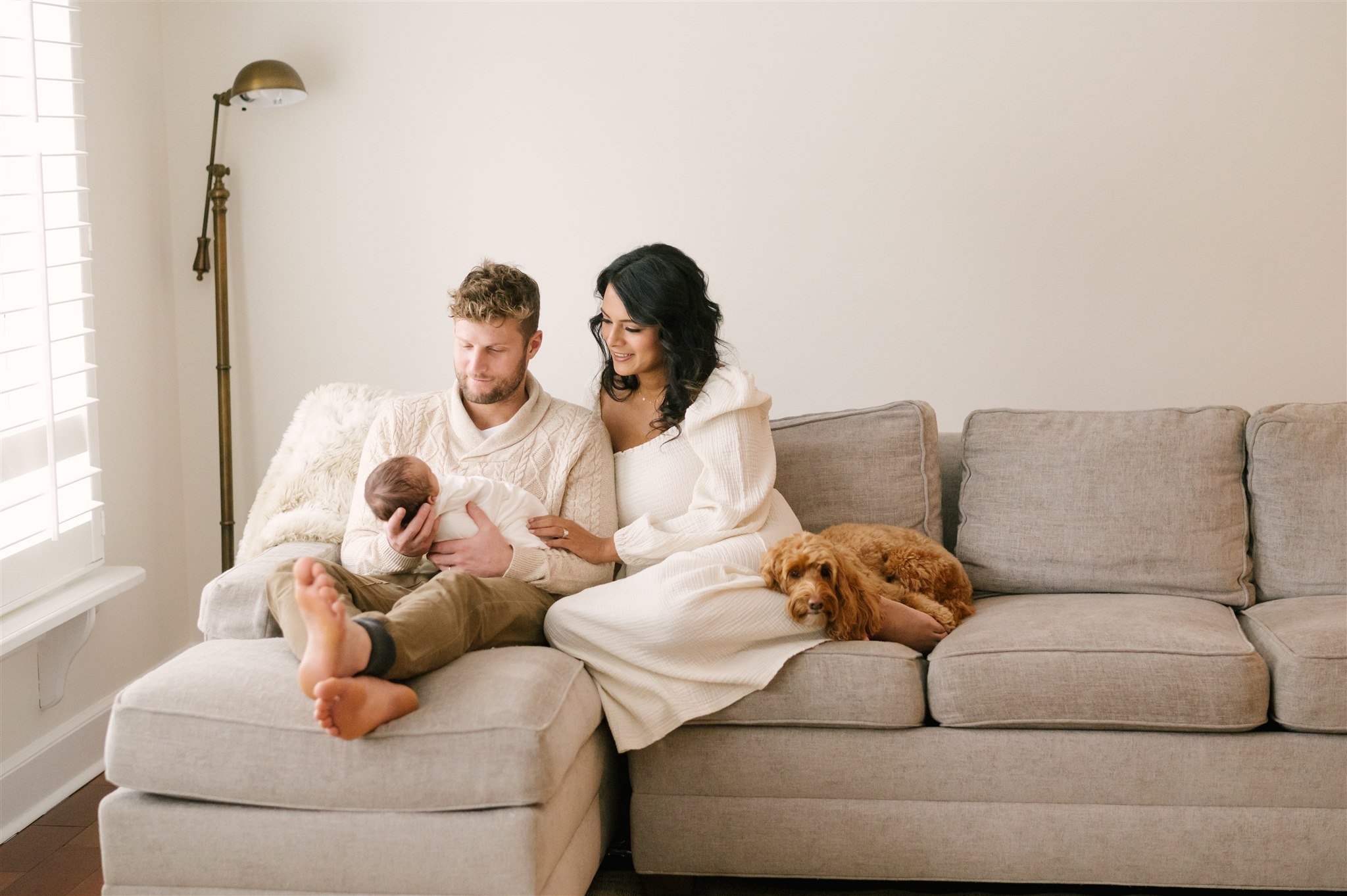 Mom and dad sitting on couch with newborn and dog during session with West Palm Beach newborn photographer