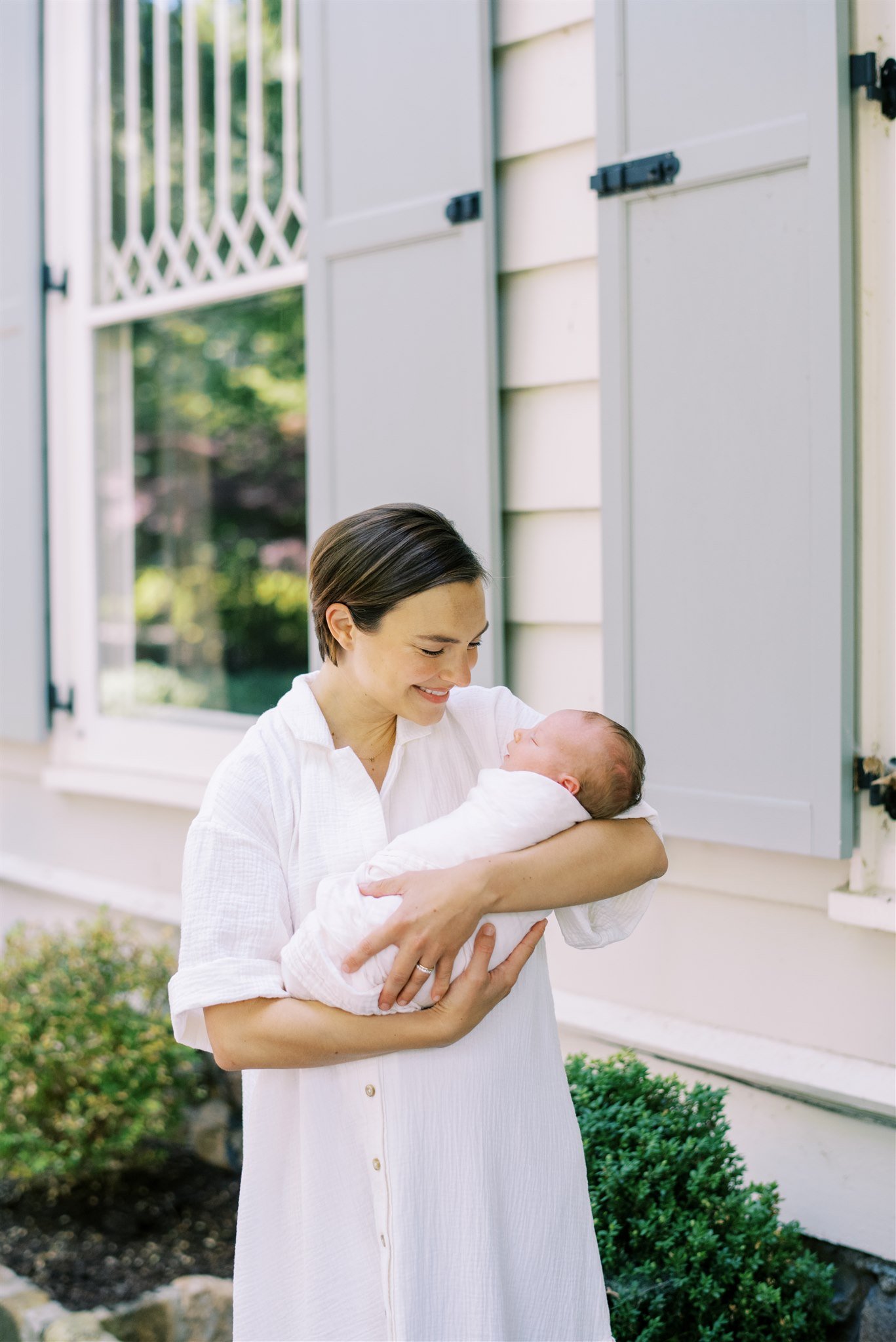Mom holding newborn in front of childhood home