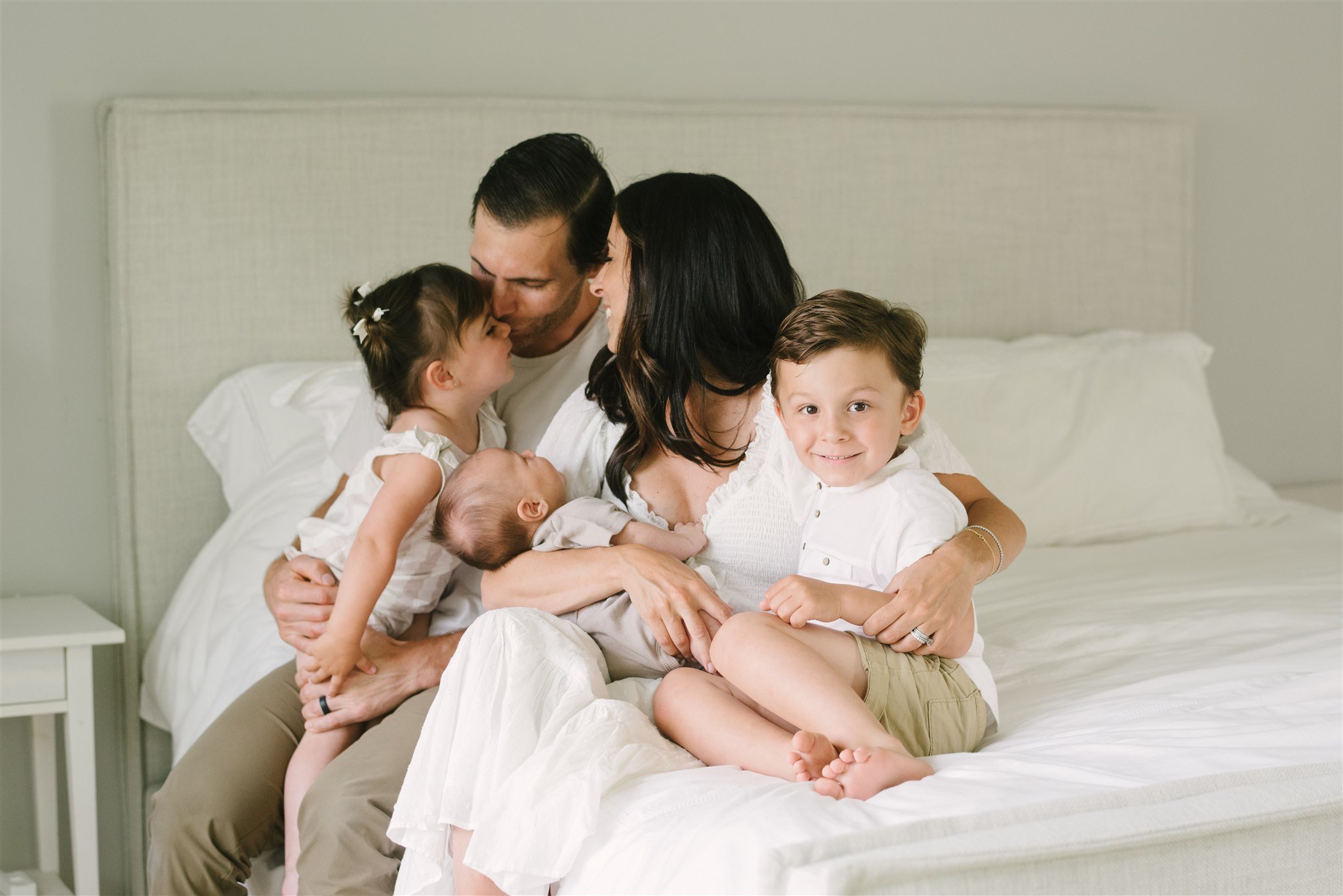 Family sitting on bed wearing white during family session