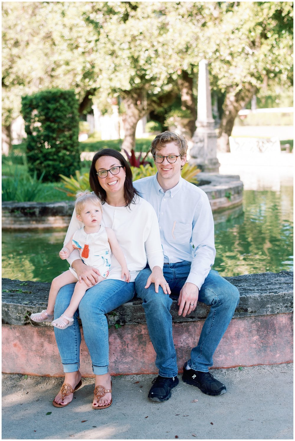Mom, dad, and daughter sitting on fountain during session with Miami photographer | NKB Photo