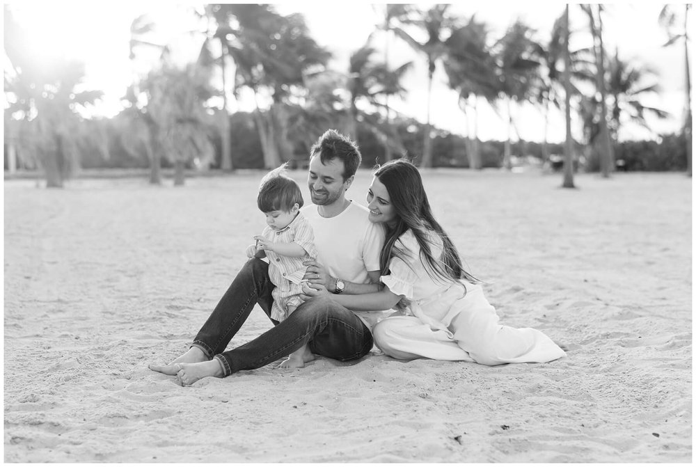 Toddler playing in sand on beach while parents sit next to him during family session | NKB Photo