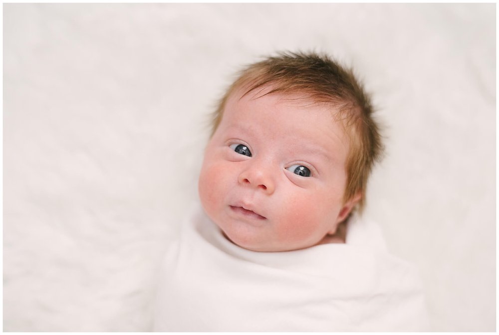 Newborn swaddled in white and looking up at camera during newborn session | NKB Photo