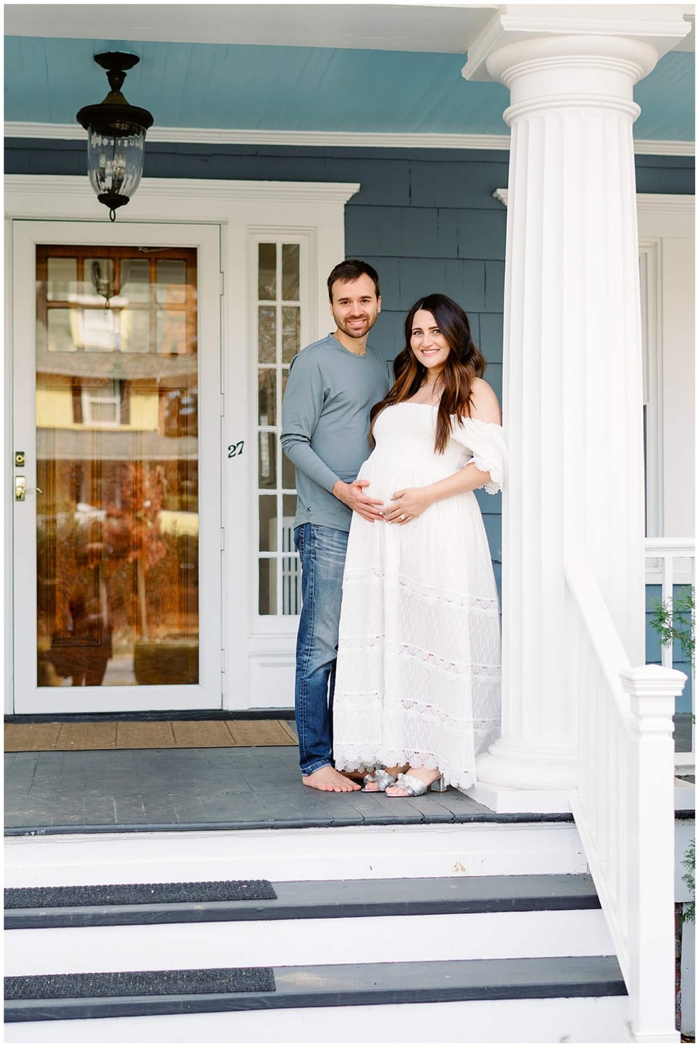 Couple standing on front porch of home during maternity session | NKB Photo