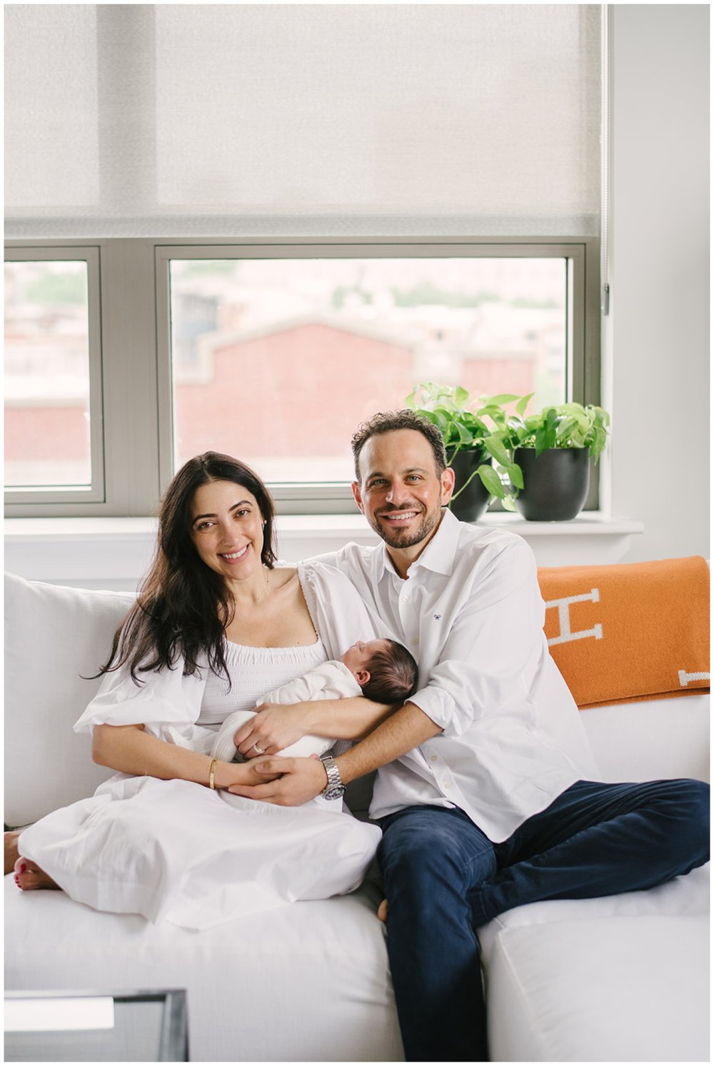 Mom and dad sitting on couch while mom holds newborn during newborn session in post about best baby stores in Boca Raton