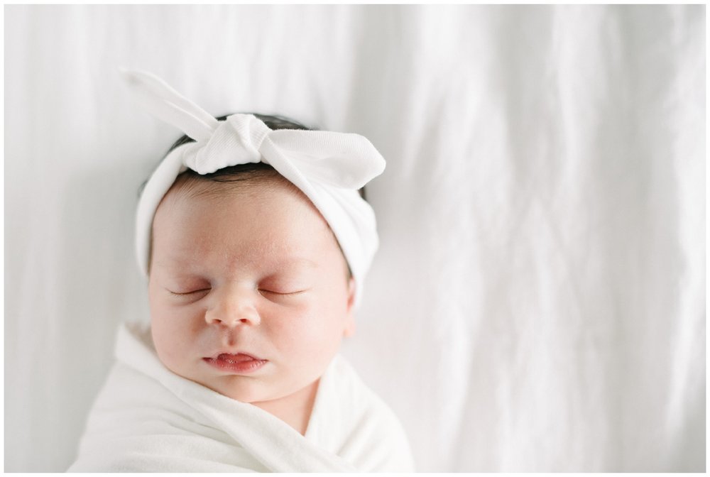 Newborn baby girl asleep in white swaddle with white bow in post about best baby stores in Boca Raton