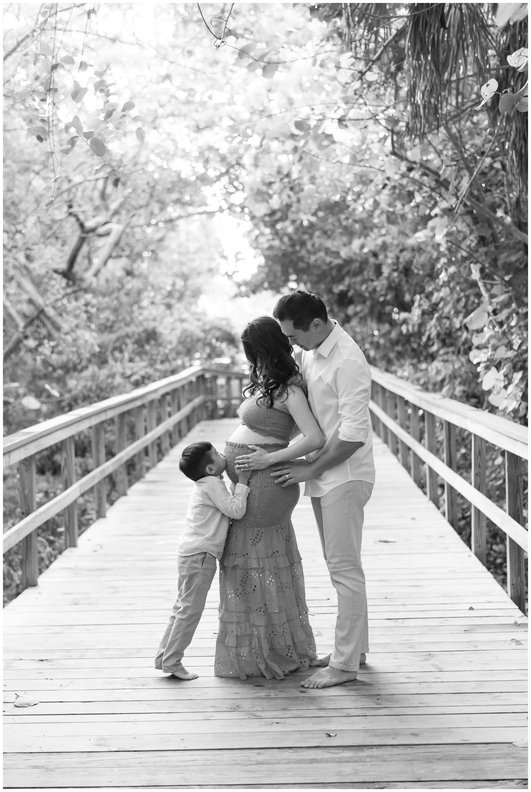 Son kissing mom's pregnant belly while mom and dad look down at him during maternity photographer in Miami | NKB Photo