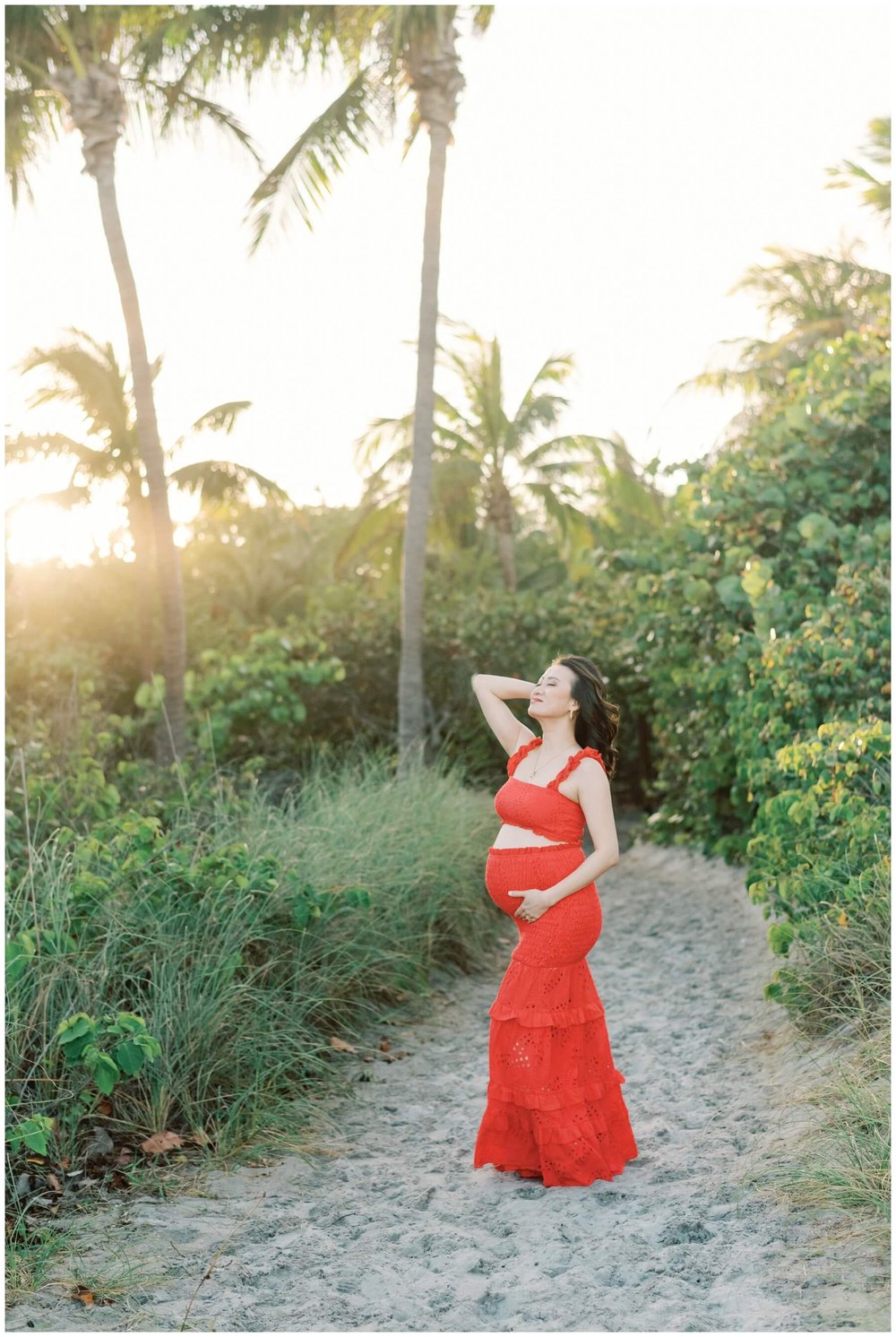 Pregnant woman wearing red outfit and leaning her head back on the beach | NKB Photo