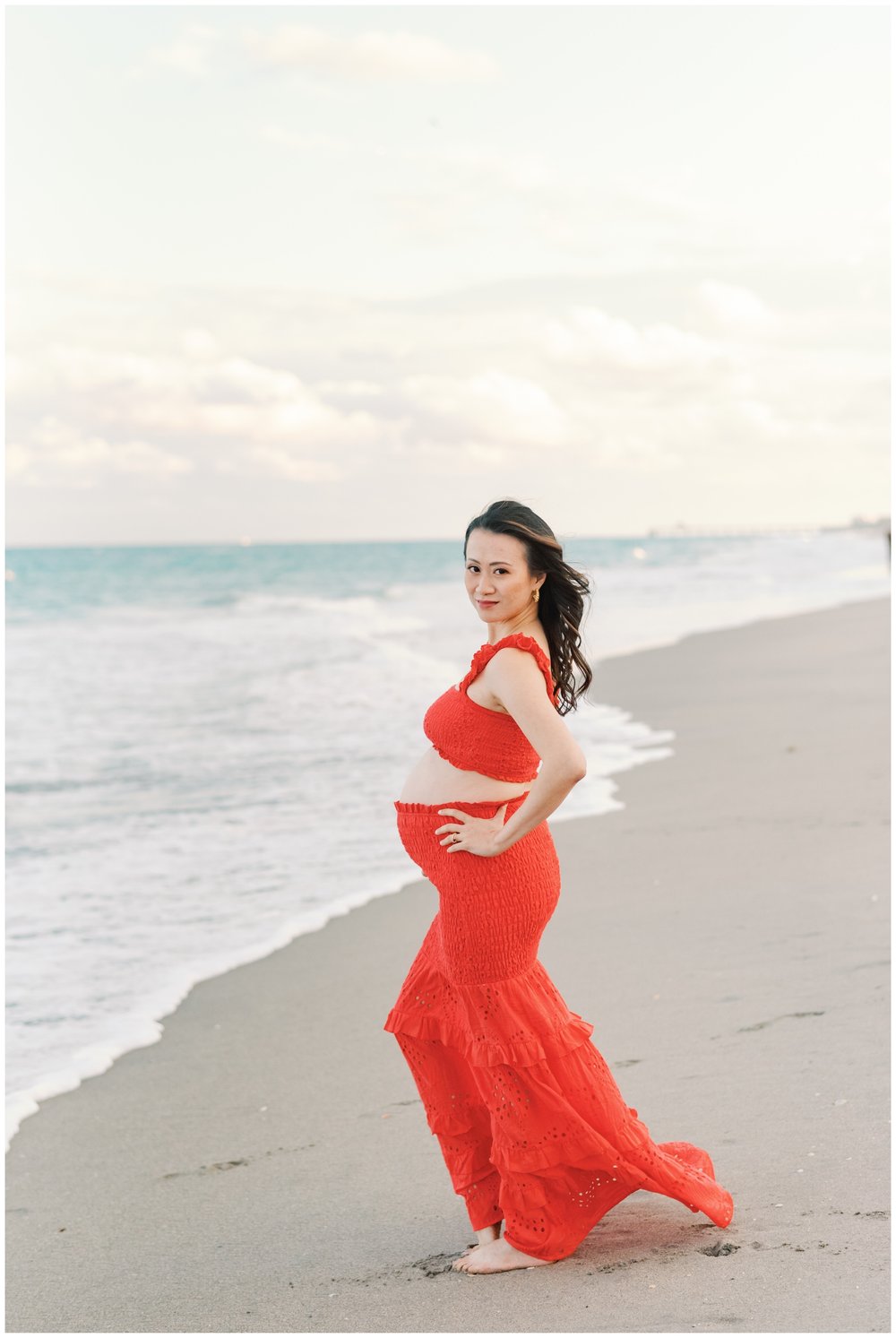 Pregnant woman wearing red two piece top and skirt taking maternity photos on the beach