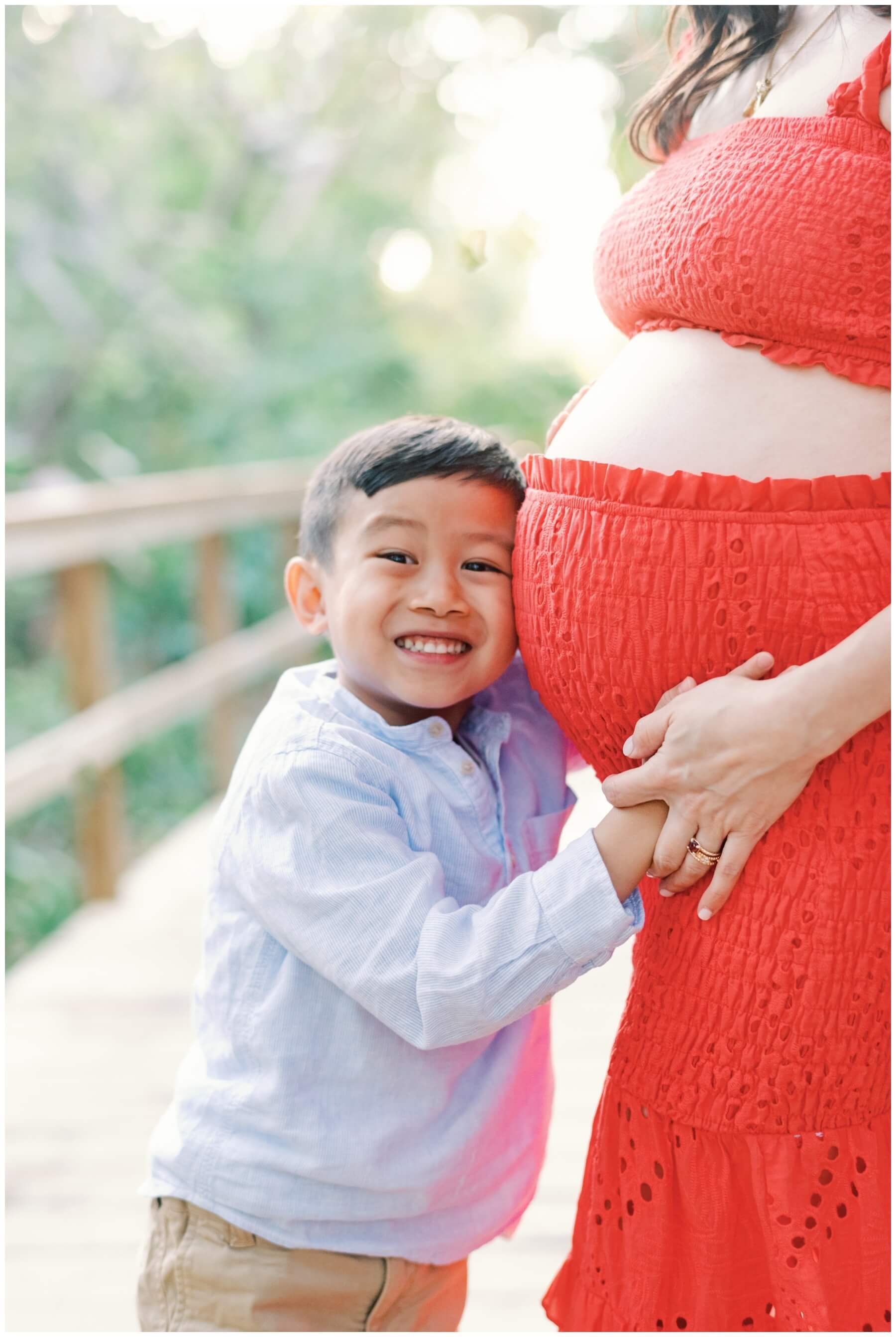Young boy leaning head against mom's pregnant belly during maternity session