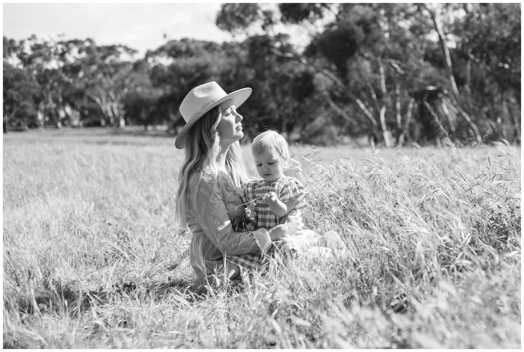 Mom sitting with young daughter in field during session with NKB Photo