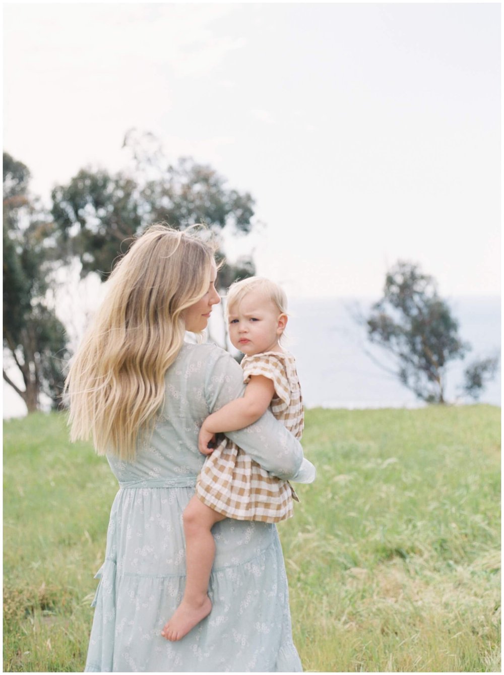 Mom holding toddler daughter in field during session with NKB Photo