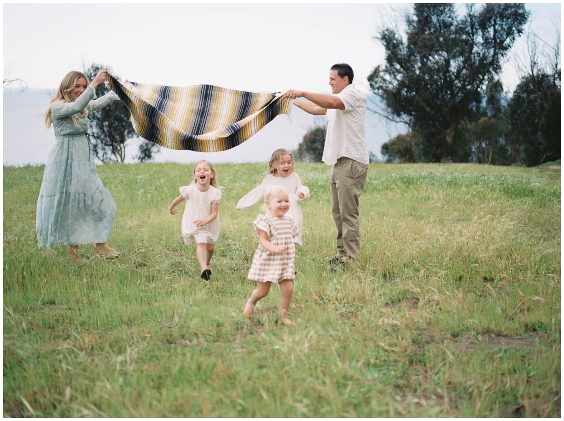 Young girls running under blanket that parents are holding in the air