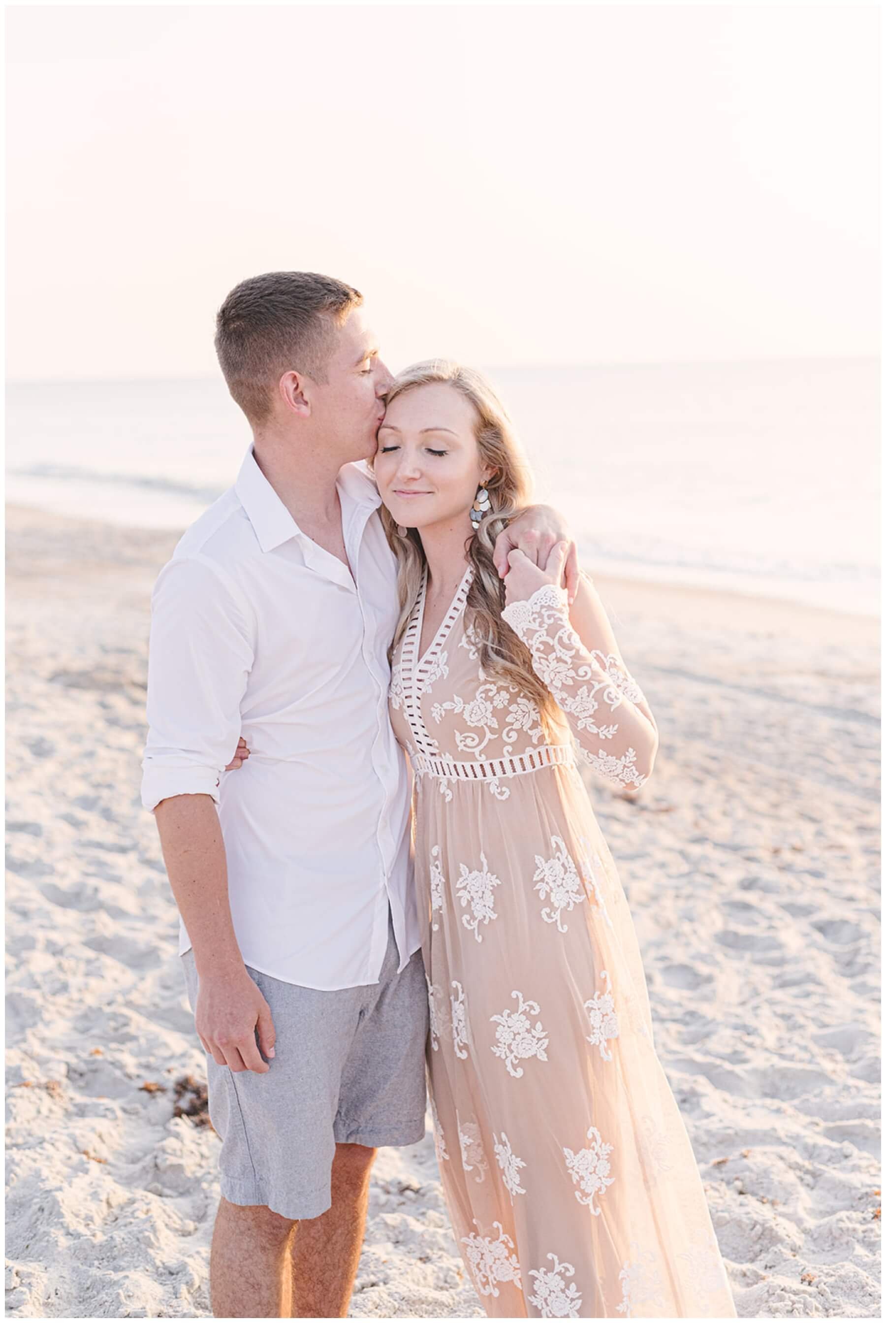 Engaged couple standing on beach and kissing during sunrise session with NKB Photo