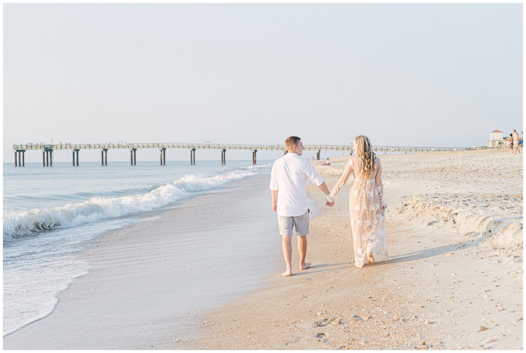 Engaged couple holding hands and walking on beach during session with NKB Photo