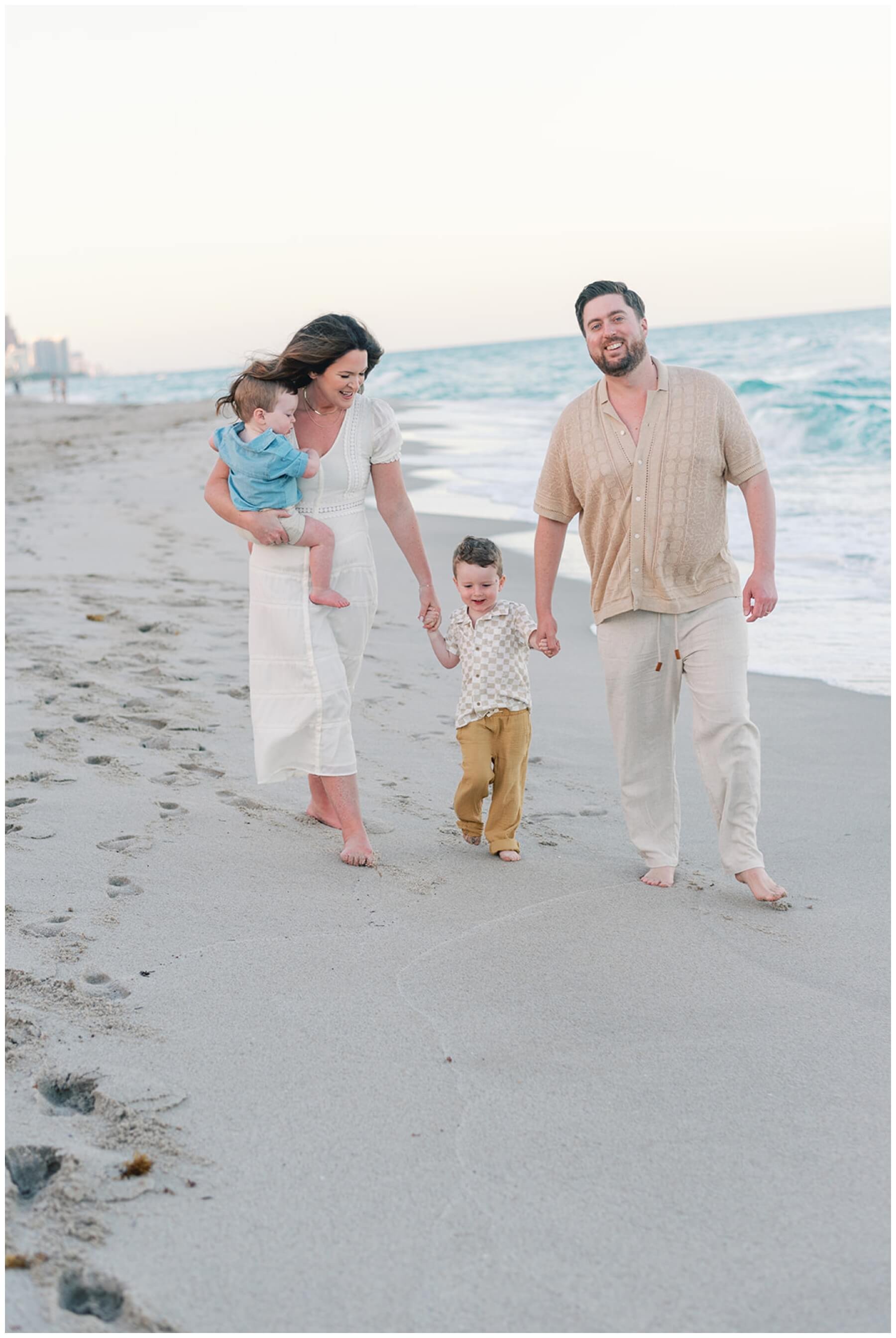 Toddler walking between parents and holding their hand on the beach | NKB Photo