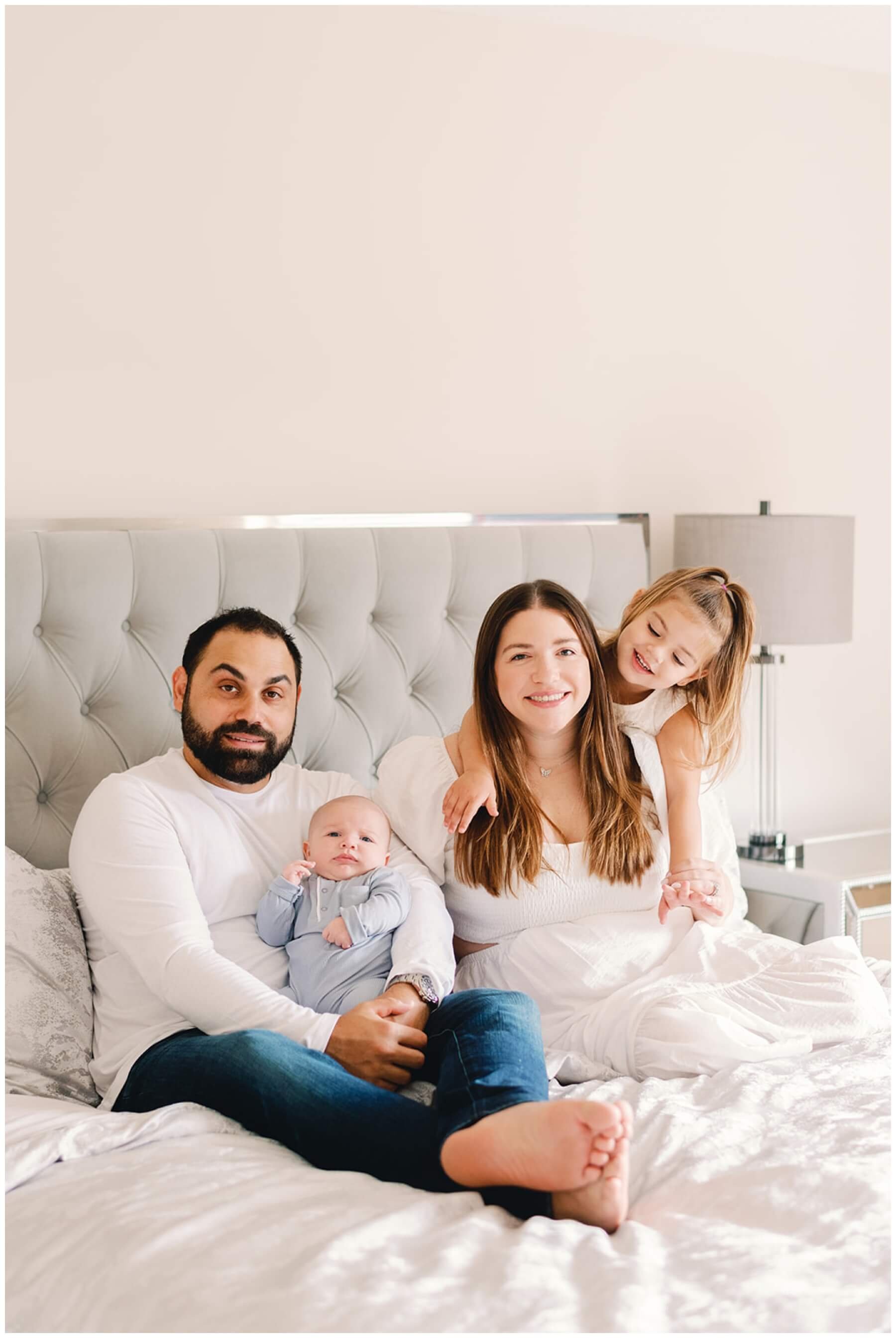 Family of four sitting on bed during newborn session | NKB Photo