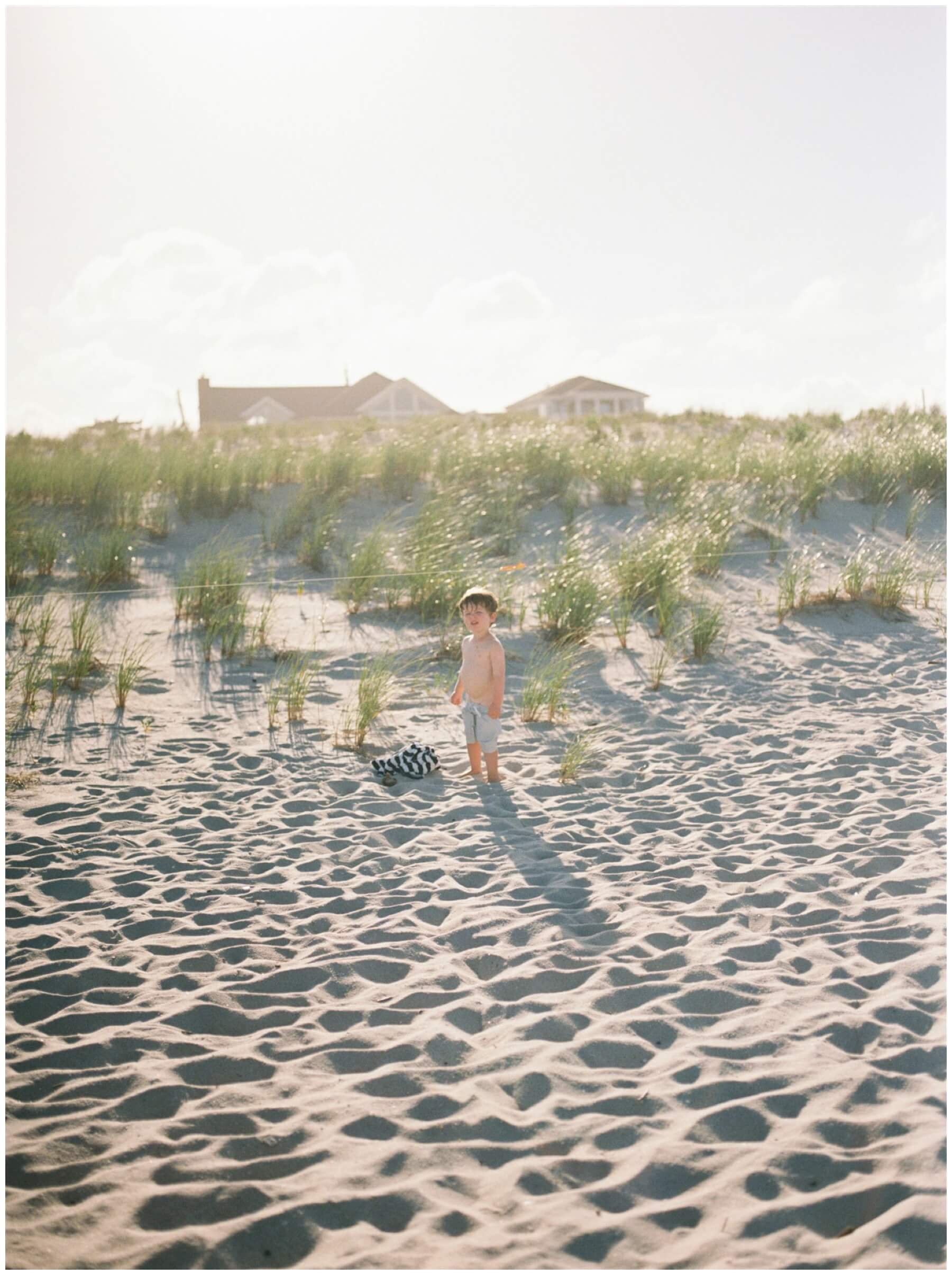 Little boy looking at camera while standing in the sand on the beach | NKB Photo