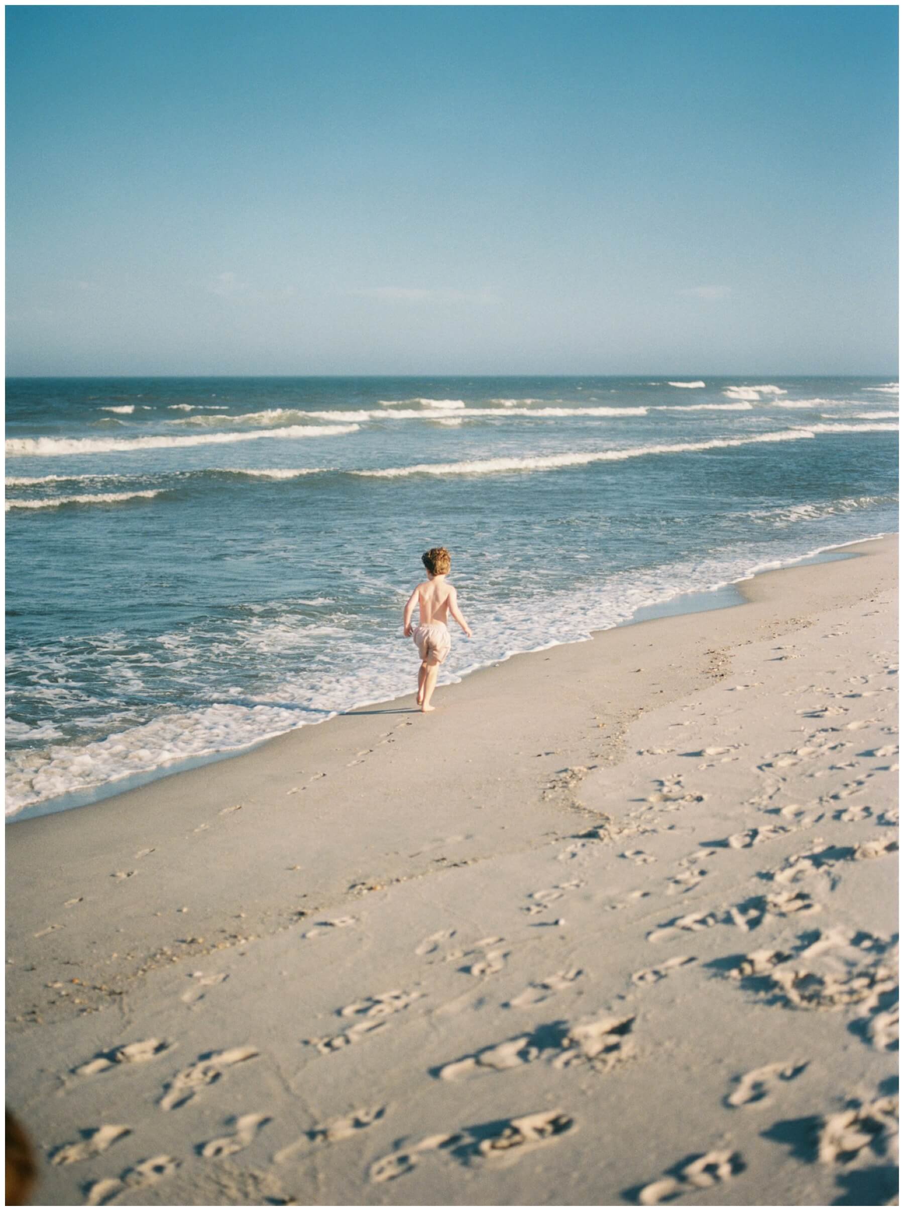 Little boy running on the sand near the ocean | NKB Photo