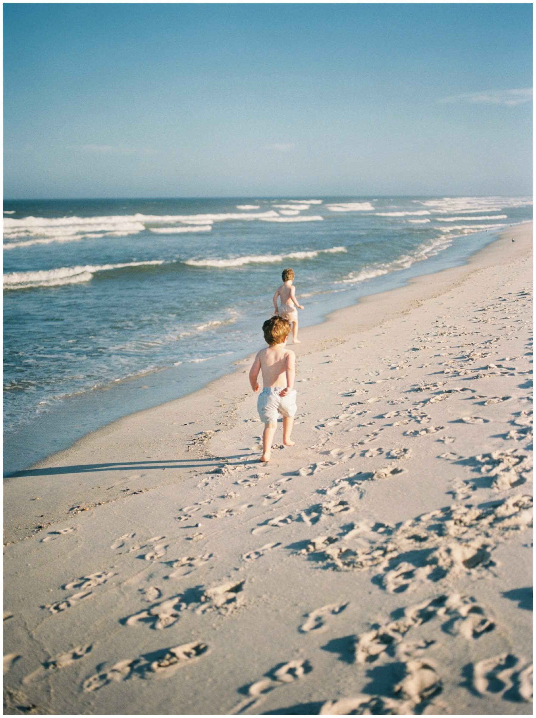 Brothers running on the sand near the ocean | NKB Photo