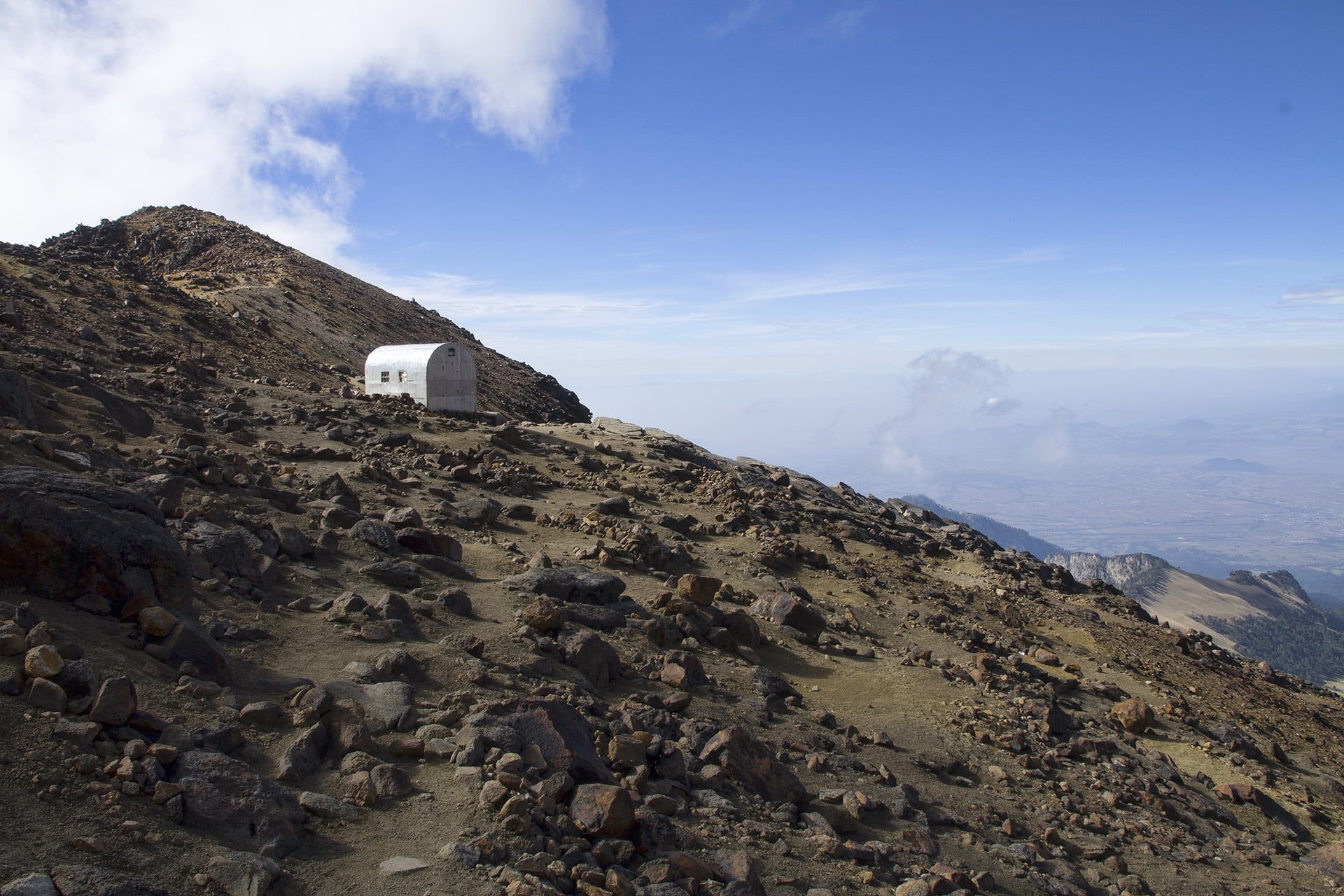  Nearing the hut reveals the terraced camp spots that years of mountaineers have sculpted upon the face of the mountain. Before collecting the gear that we had left in the hut, we take some time to make tea and instant pasta. A man wearing tennis sho