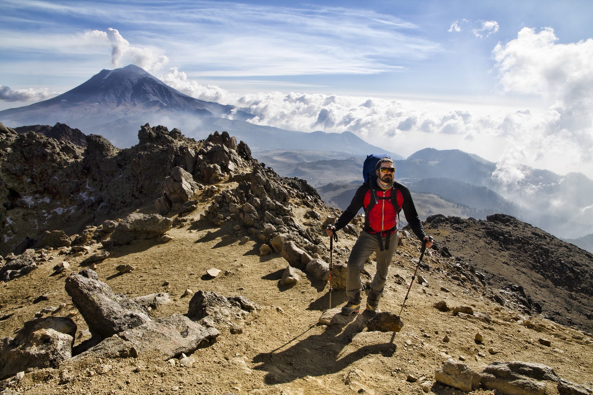  An irritated Popocatépetl launches tufts of smoke into the atmosphere, then fall back down to a more stable elevation far below the summit. Rippling cirrus clouds seem to emanate outward from the axis of the crater. 