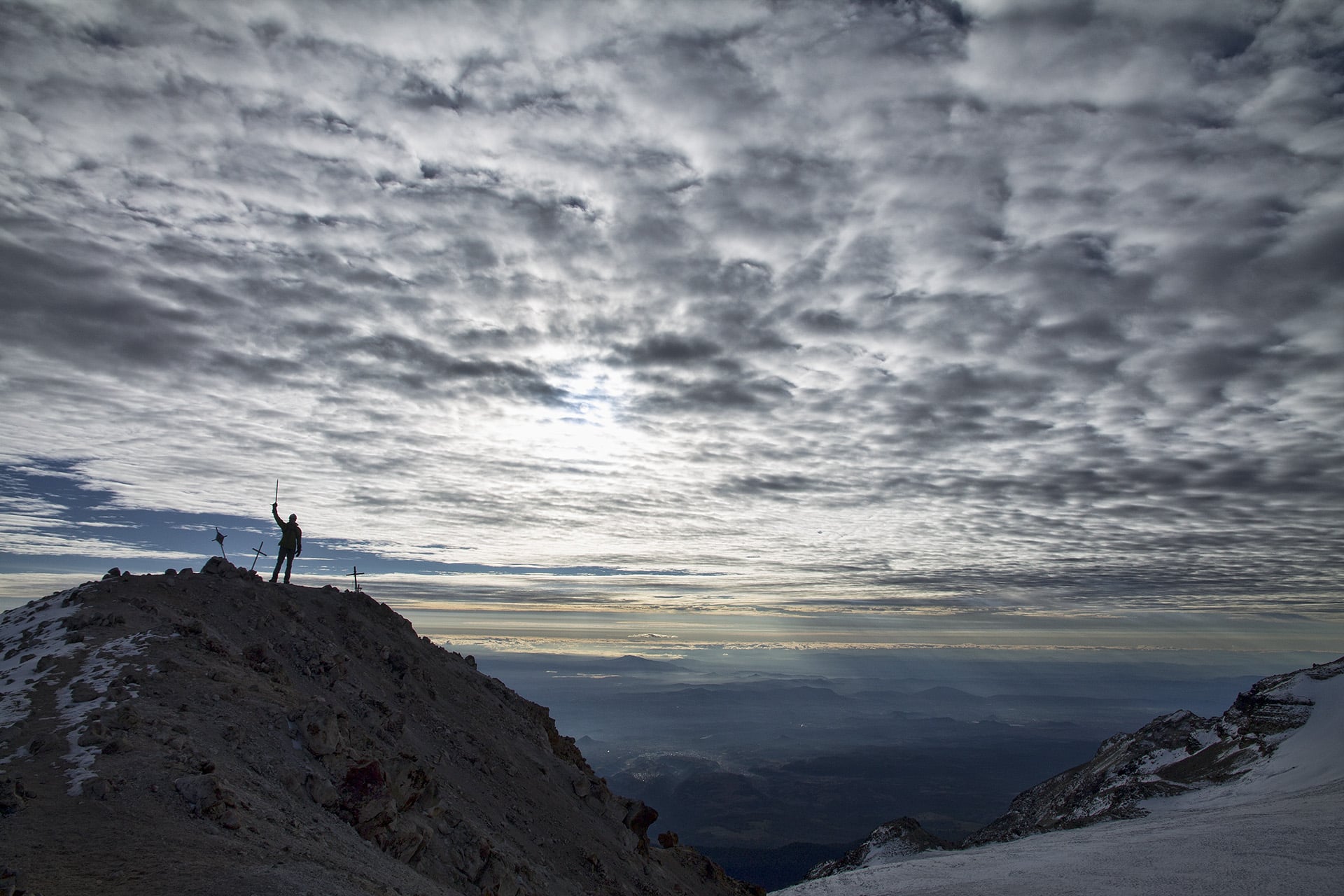  I look up toward the end of the ridgeline I am now following. My brother’s silhouette is backlit with axe raised amongst a garden of tilted summit crosses.&nbsp; 