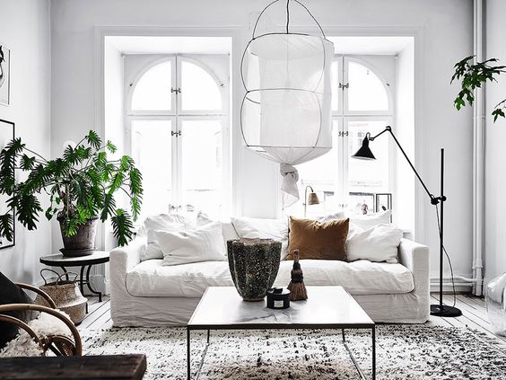 The amount of light flooding into this apartment, simple white rustic poufy sofa, a rocking cane chair and a plain white wall full of art with a beautiful old carpet, that says come on down onto the floor = happiness. Those green leafy highlight complete this already charming space to perfection. not entirely sure how we feel about the light fixtures, but we love this space enough to have two pictures from diff angles.