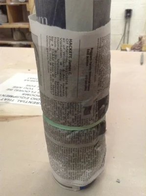 The clay slip is inside the outer sleeve of newspaper, where the darker, wetter area can be seen. The rubber band is holding the layer shut, but also adding its own wrinkle pattern to the paper and clay.