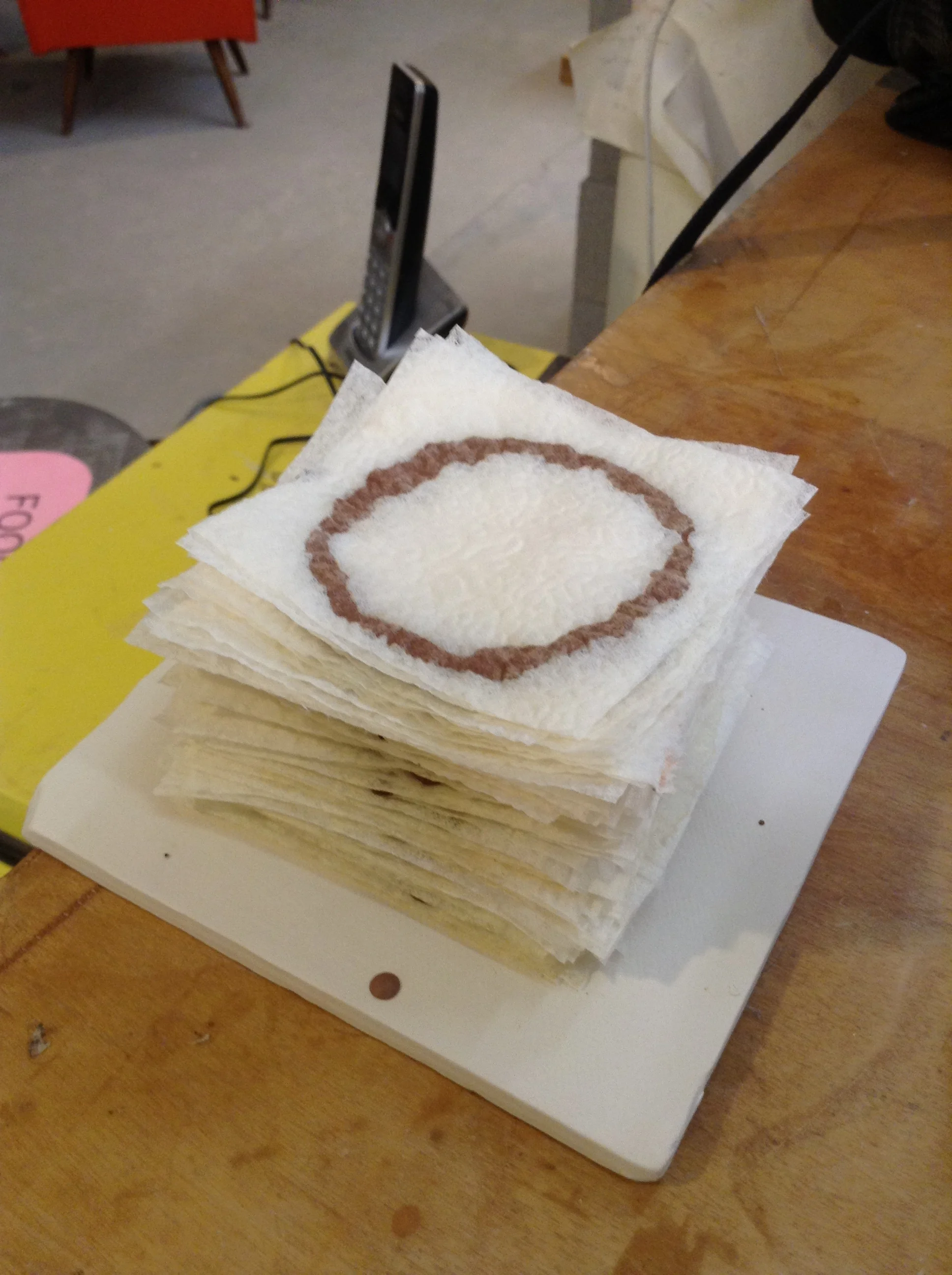 Examples of clay slip used in its most runny form, unalterd from the consistency bought for slip casting in plaster molds. Single napkin layers cut into squares stabilize hand-squeezed clay lines. Small textures of paper transferred to clay while liquid. The paper squares do shift a bit, which might be important enough to prevent. Drawing the lines with the squeeze bottle sometimes touches the nozzle to the paper, dragging it a little because the immediately previous layer is still soft. The fix is to not touch the nozzle to the paper. Actually holding the paper steady --say, from a corner-- is actually too subtle because even that little pressure squeezes further the line underneath. Not that it's undesirable.