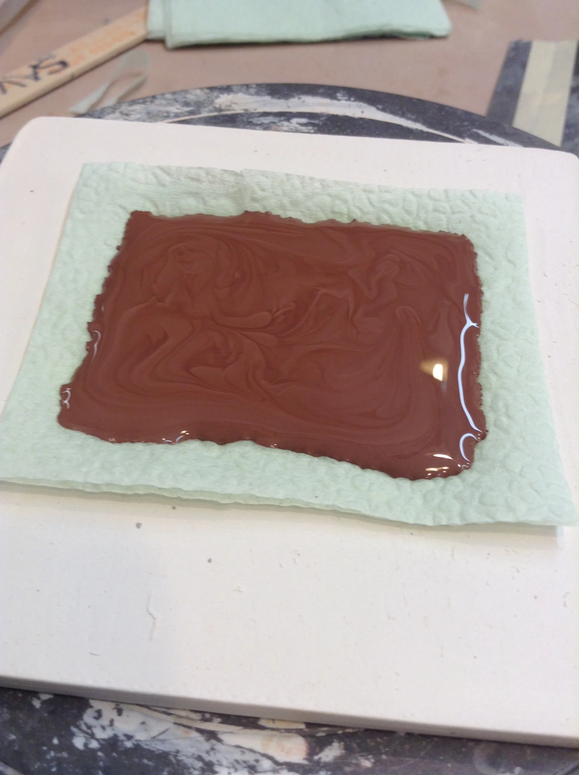 Red earthenware slip pooled into a square shape on napkin tissue. It takes a few minutes for it to set up a little on the bottom, but as pictured, would drip off the top if tilted too far. Conveniently, anything placed on this wet surface would adhere permanently.