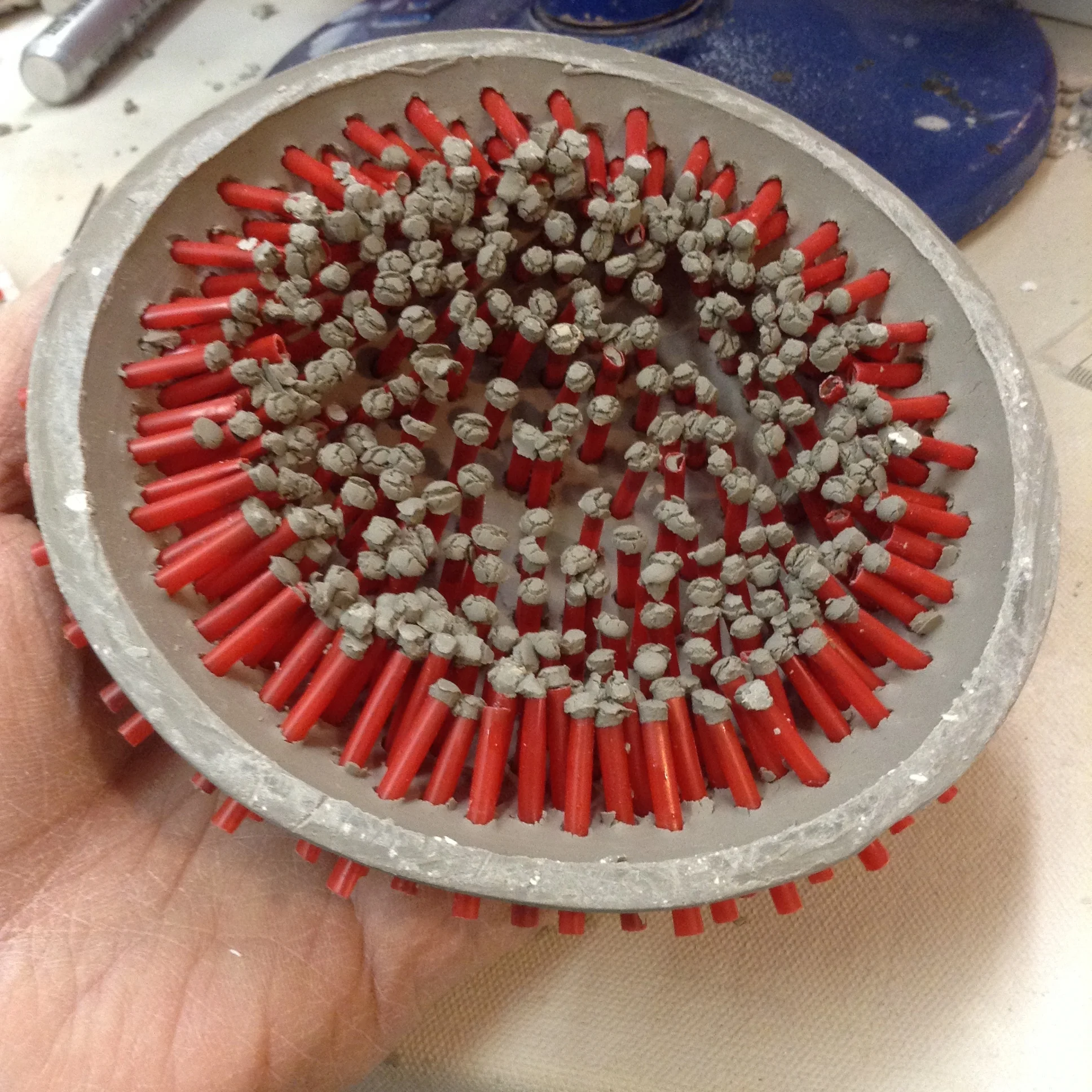 Interior of plaster dome forming bowl. All these ends of coffee stirrers will be completely enclosed in plaster, which eventually is used to hold nails. Conveniently, pushing the straws through the clay wall left a little plug of clay on the ends, which prevents most of the plaster from draining out.