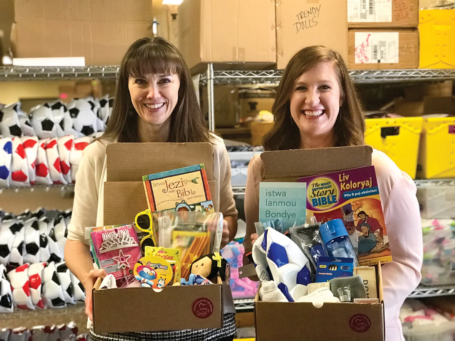 Christy Dillon and Molly Knost hold samples of the pre-paid shoeboxes we pack (age-specific) on your behalf. Order them online at shoeboxdrive.com.