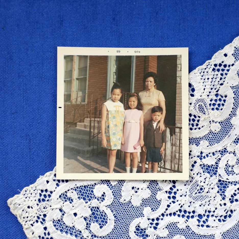 old photograph from 1968 showing an asian mother with her three school-aged children standing in front of cement steps outside a brick house
