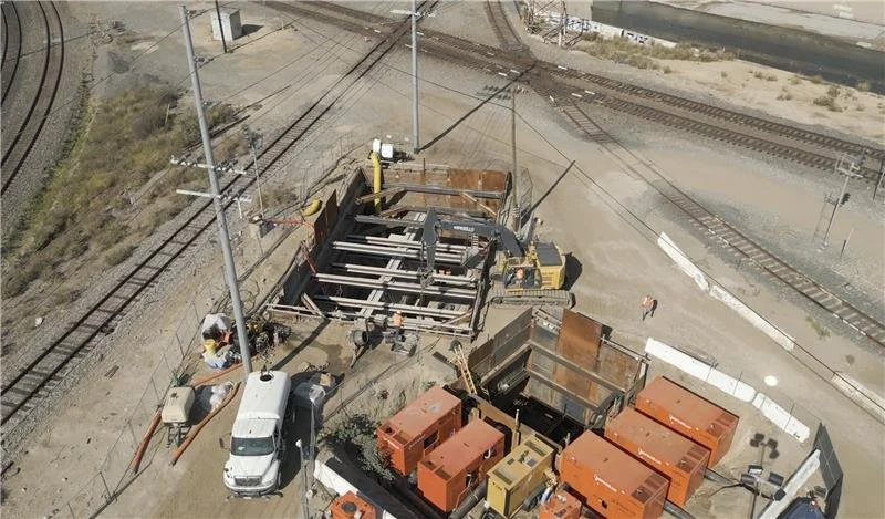 Construction site near train tracks with machinery, containers, and workers.