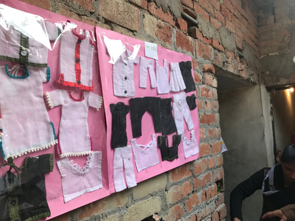 Small scale models of clothing articles hang on the wall to give sewing students an example to follow. 