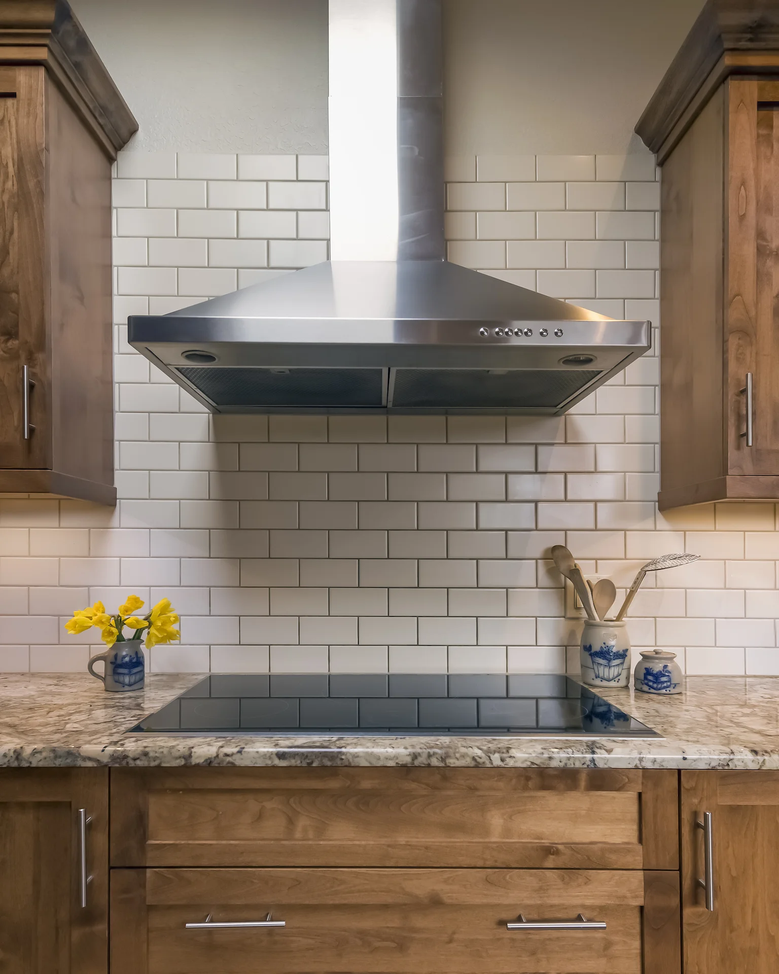 Simple, cream subway tile, a sleek induction stove and stainless steel hood create a simple backdrop for all the different wood species in the kitchen. &nbsp;