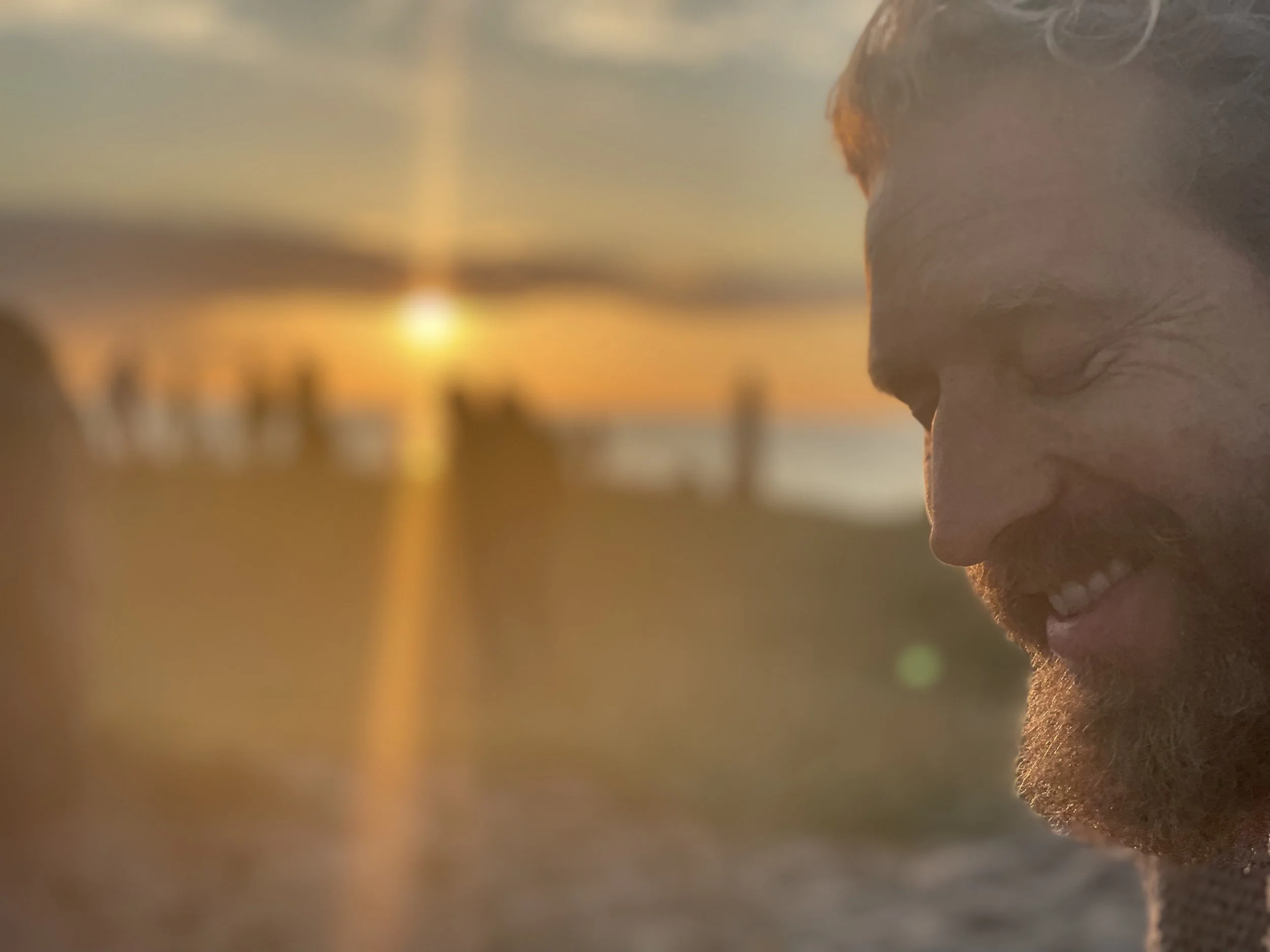 A relaxed and smiling founder with a sunset, ocean and other people in the backdrop